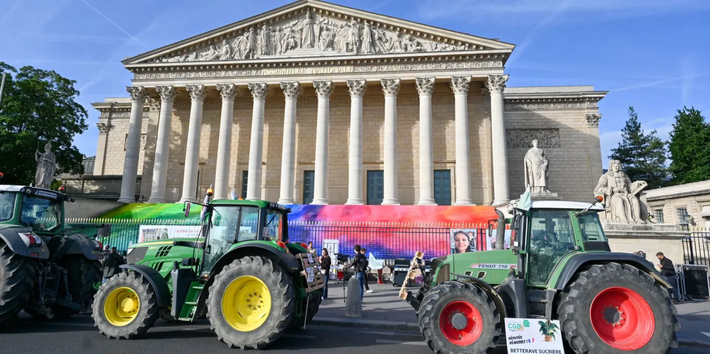 Tracteurs garés devant la façade de l'Assemblée nationale lors d'un rassemblement agricole, avec une pancarte mentionnant la betterave sucrière.