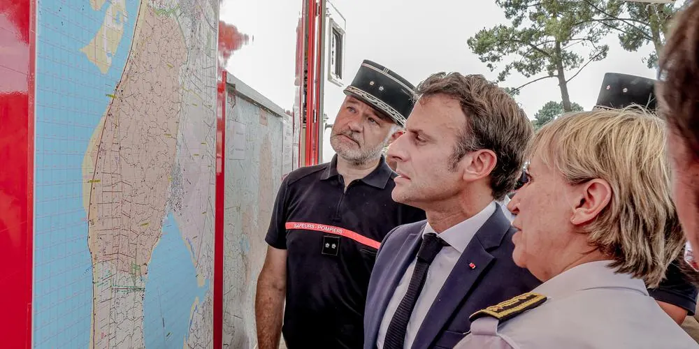 Un homme en costume, entouré d'officiers de sapeurs-pompiers en uniforme, examine une grande carte du littoral affichée sur un camion.