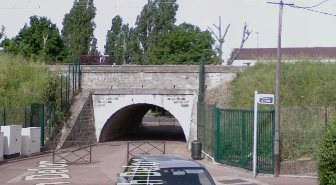 Vue actuelle du pont du RER B à Antony : une arche de pierre sous le talus de la voie ferrée, encadrée de grilles vertes, ouvre un passage piéton.