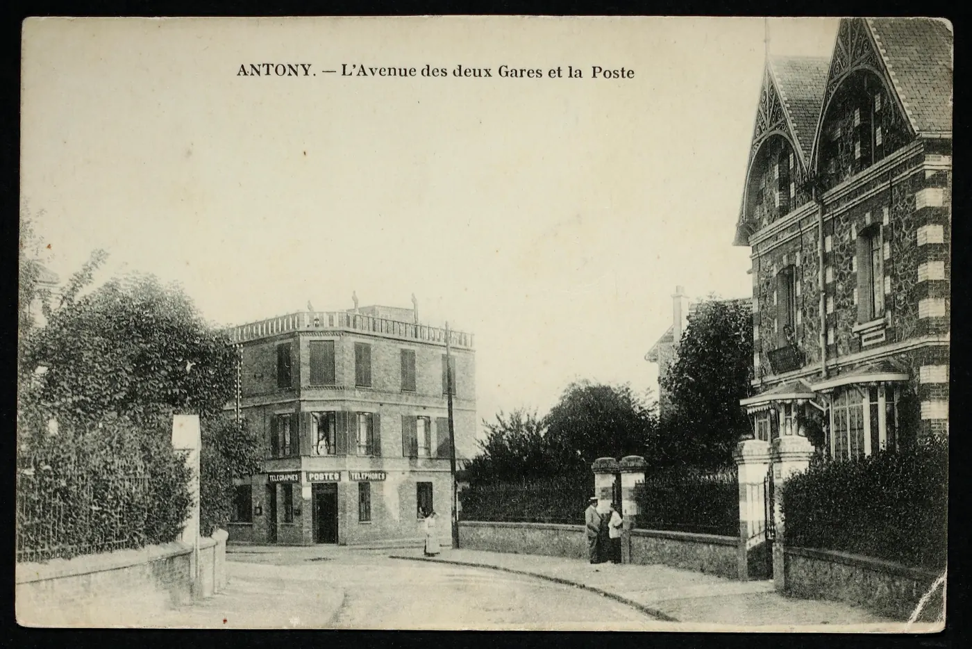 Carte postale ancienne « Antony, l'avenue des deux Gares et la Poste » : le même virage, avec la poste dans l'immeuble d'angle et la maison à pignons ouvragés à droite.